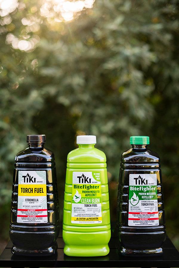 Three TIKI Brand torch fuel bottles, including BiteFighter mosquito repellent and citronella, displayed outdoors.