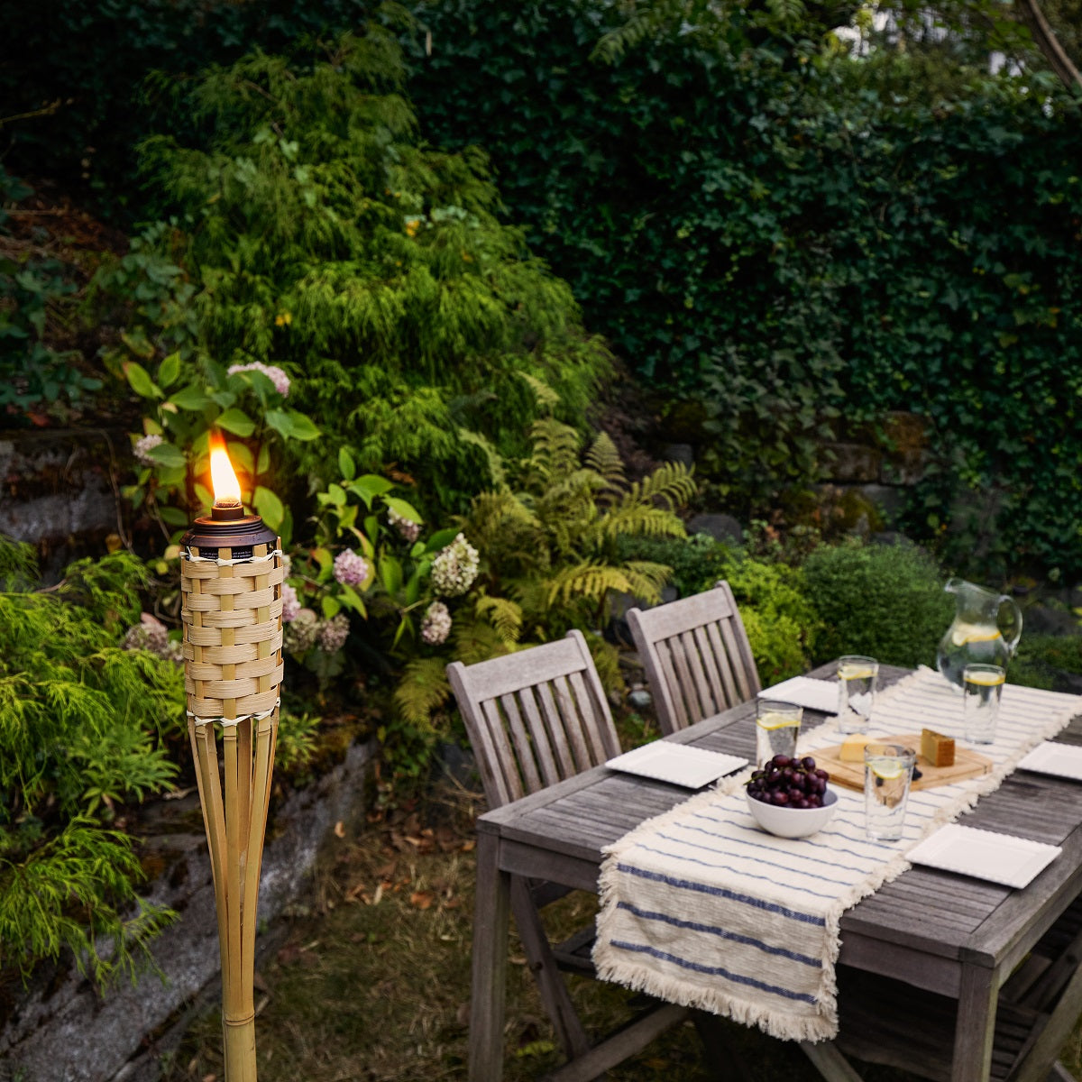 Natural woven torch with flame, outdoor dining setup.