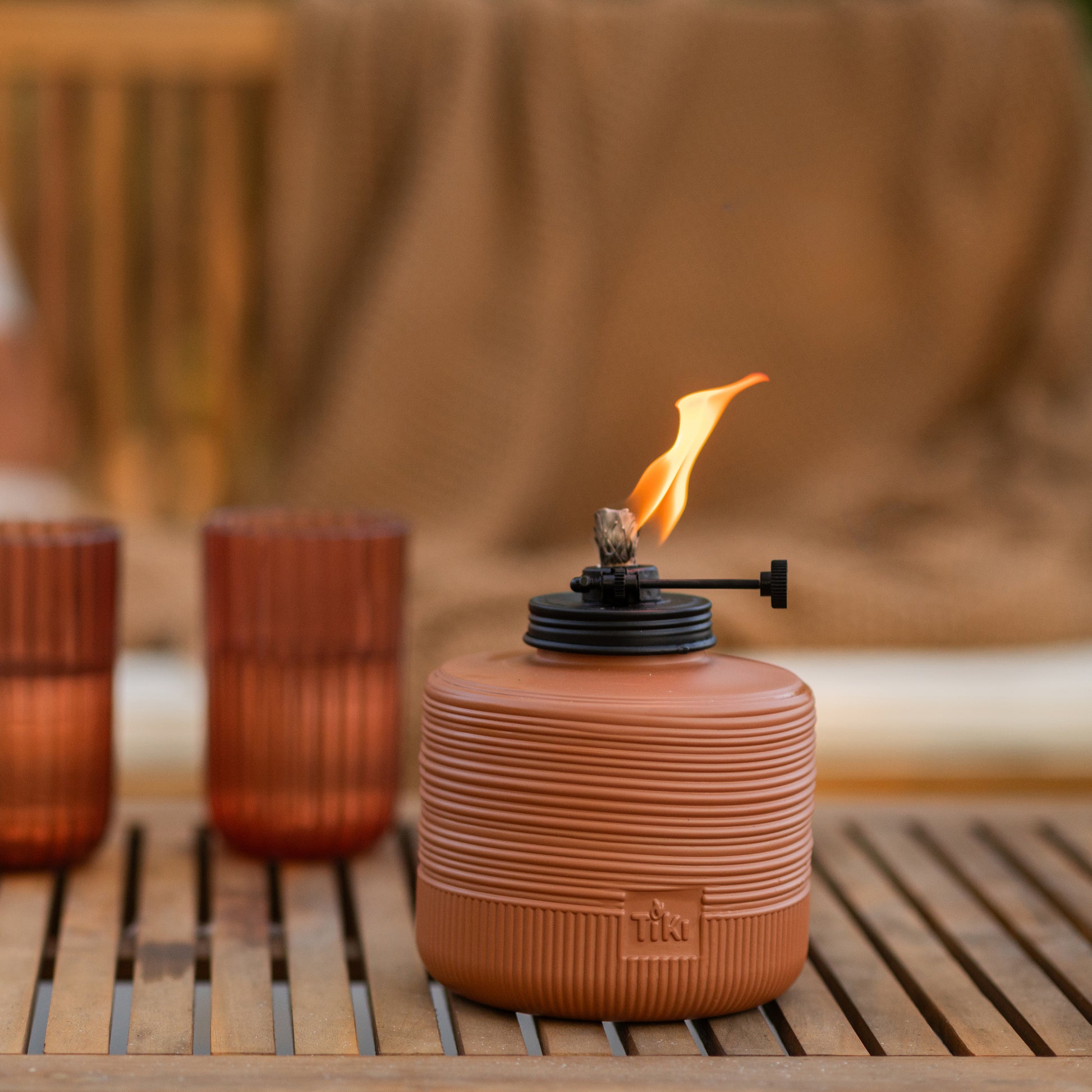 Orange Tiki torch with flame, set on wooden surface.
