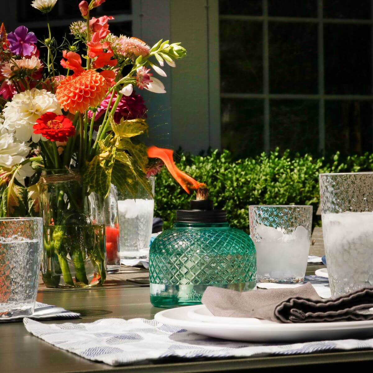 Green glass lantern with orange flame, set on table with floral arrangement and glasses.
