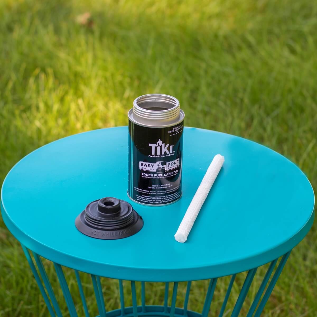 Black TIKI Easy Pour Torch Fuel Canister with cap and wick on blue table.
