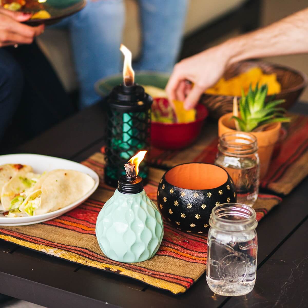 Green ceramic oil lamp with textured design, lit flame, on colorful table setting.