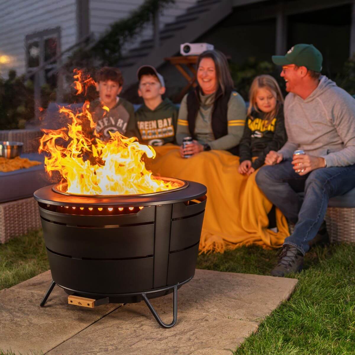 Black outdoor fire pit with glowing flames, surrounded by a family enjoying a cozy evening.