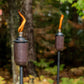Brown Tiki torches with orange flames, outdoor setting.