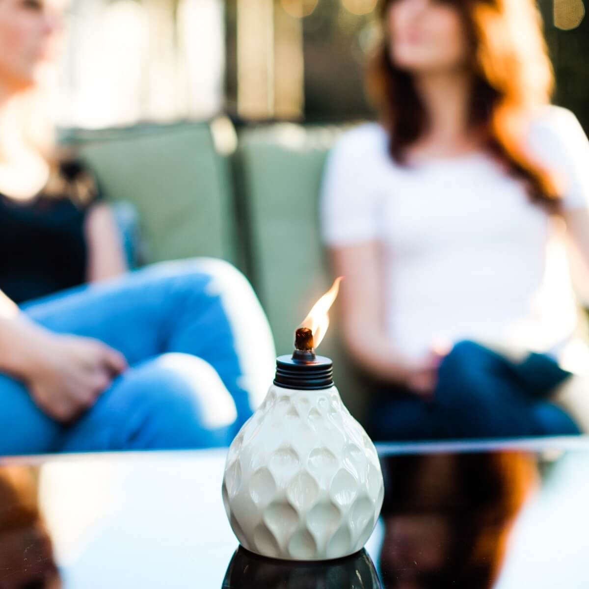 White textured oil lamp with flame, sitting on table.