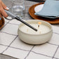 White Tiki triple-wick candle being extinguished with a gray candle snuffer.