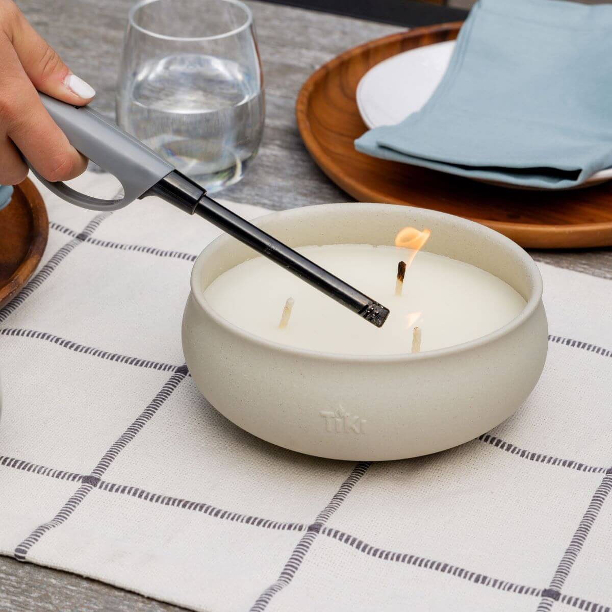 White Tiki triple-wick candle being extinguished with a gray candle snuffer.
