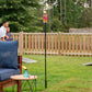 Glass tiki torch on a tall black pole, lit with a visible flame, set in a grassy backyard near outdoor seating.