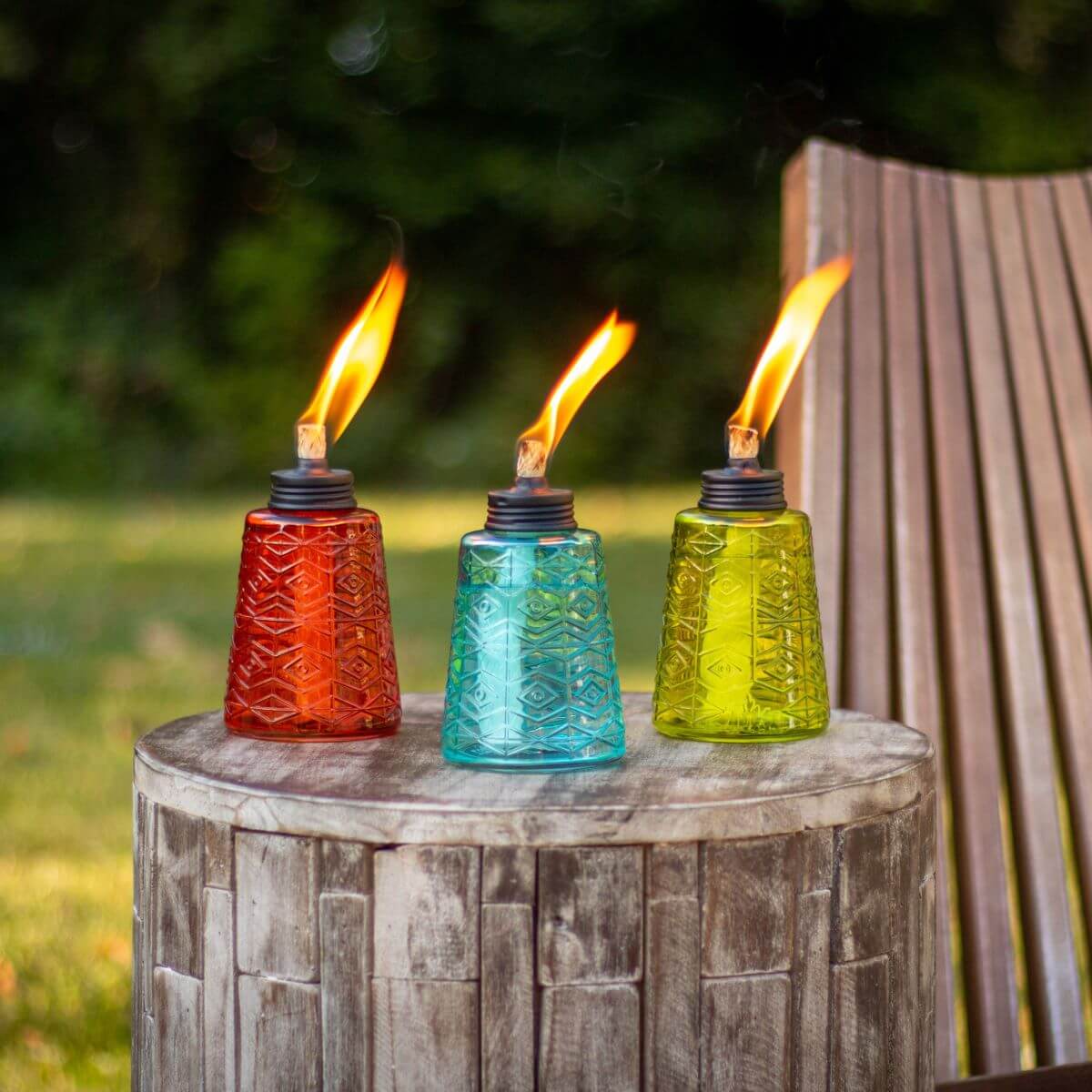Colorful glass tiki torches in red, blue, and green with flame, outdoors.
