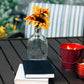 Clear glass vase with sunflower, red bucket candle, and stacked books on table.