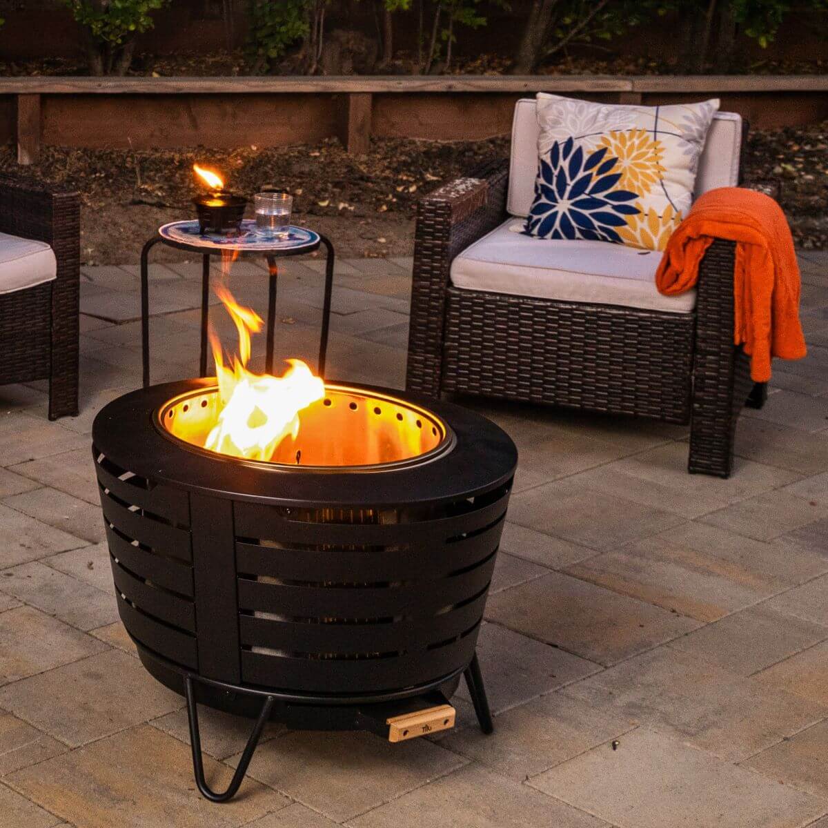 Black outdoor fire pit with wicker furniture and decorative pillows.