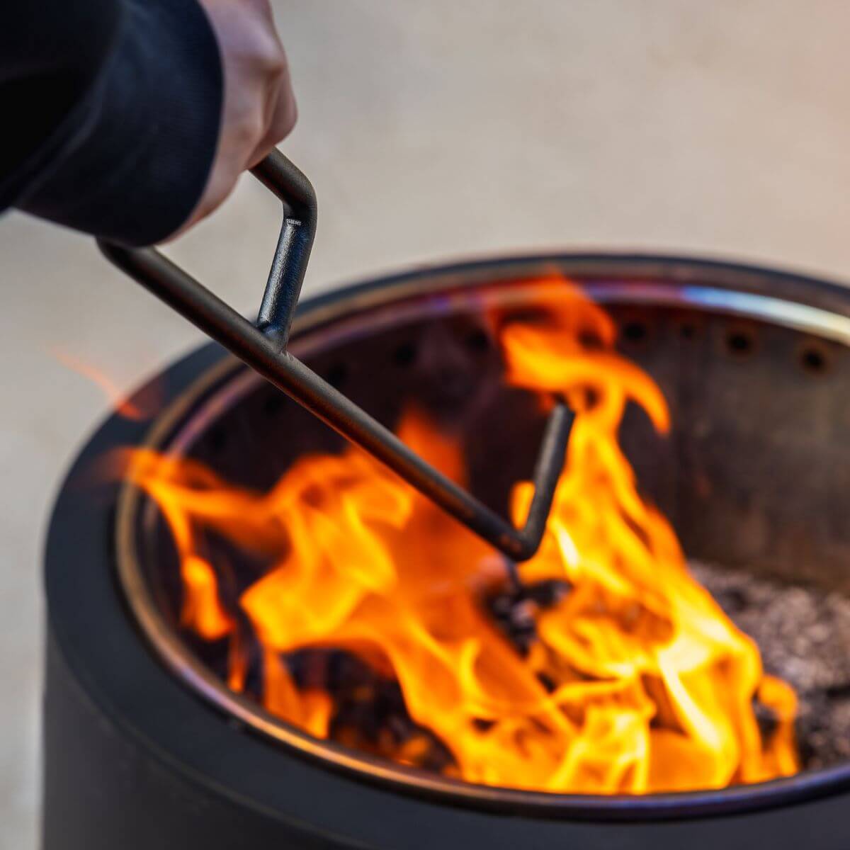 Black portable fire pit with handle, glowing orange flames inside.