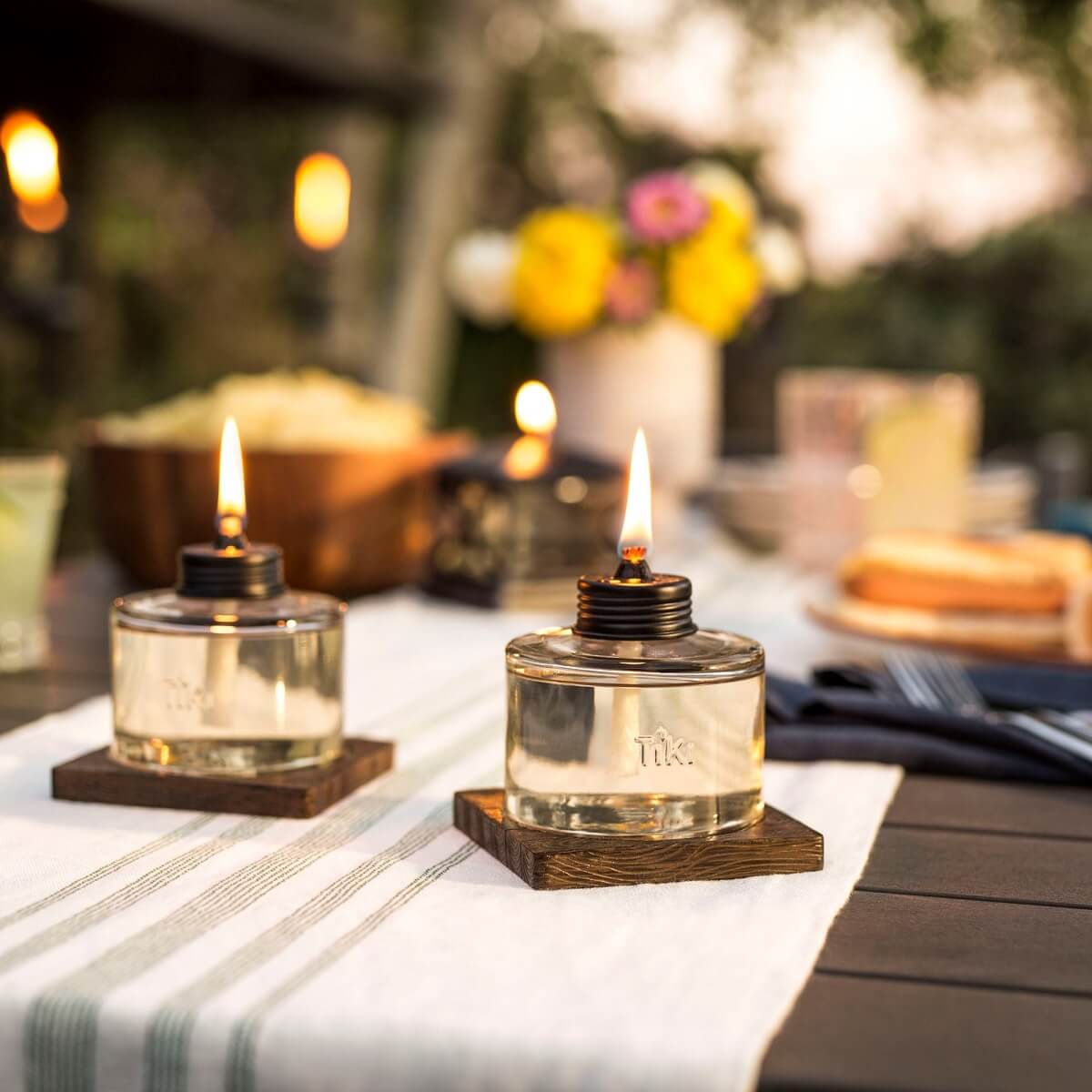 Clear glass Tik oil lamps with wooden bases, lit on a table setting.