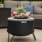 Black round outdoor fire pit table with gray top, surrounded by wicker furniture and decorative items.
