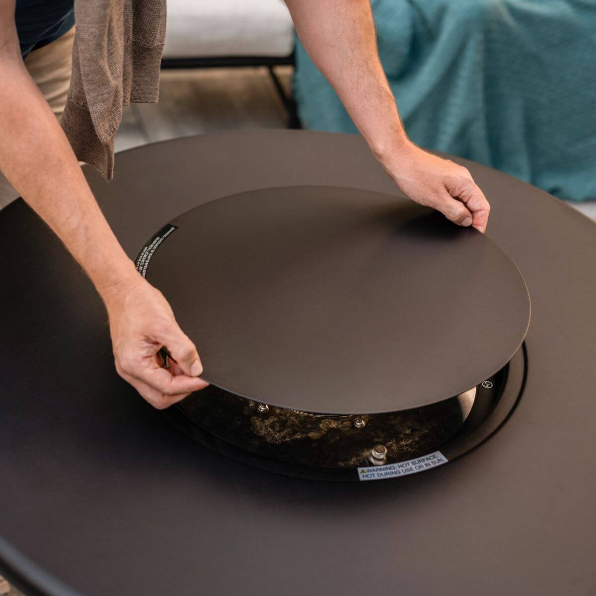 Black round electric griddle with warning label, being adjusted by hands.