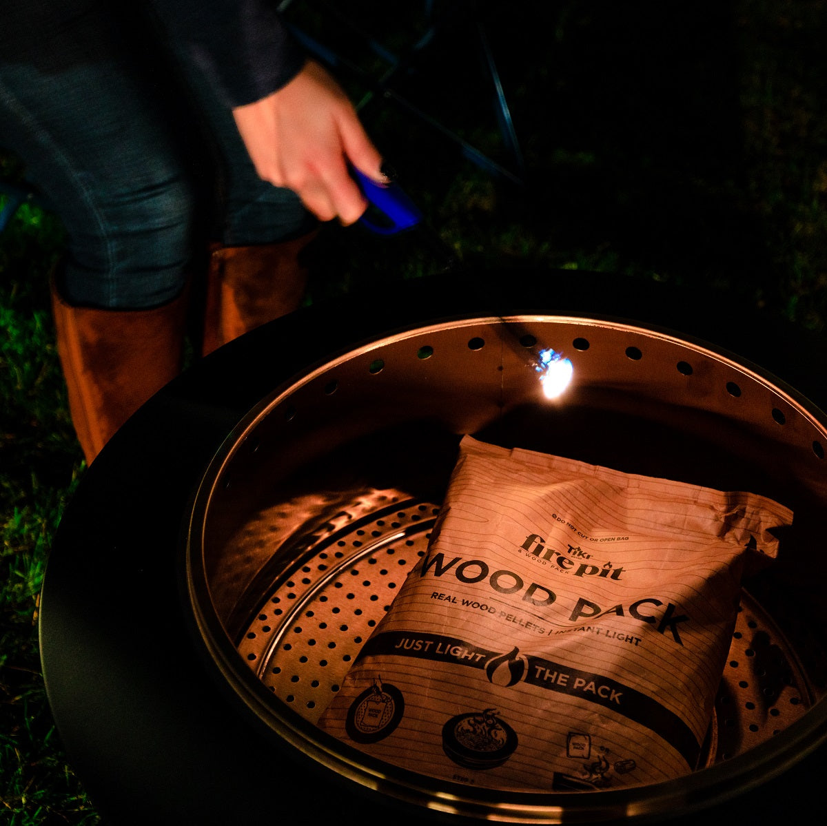 Brown Firepit wood pellet pack with "Just Light the Pack" text, being lit with a blue lighter.