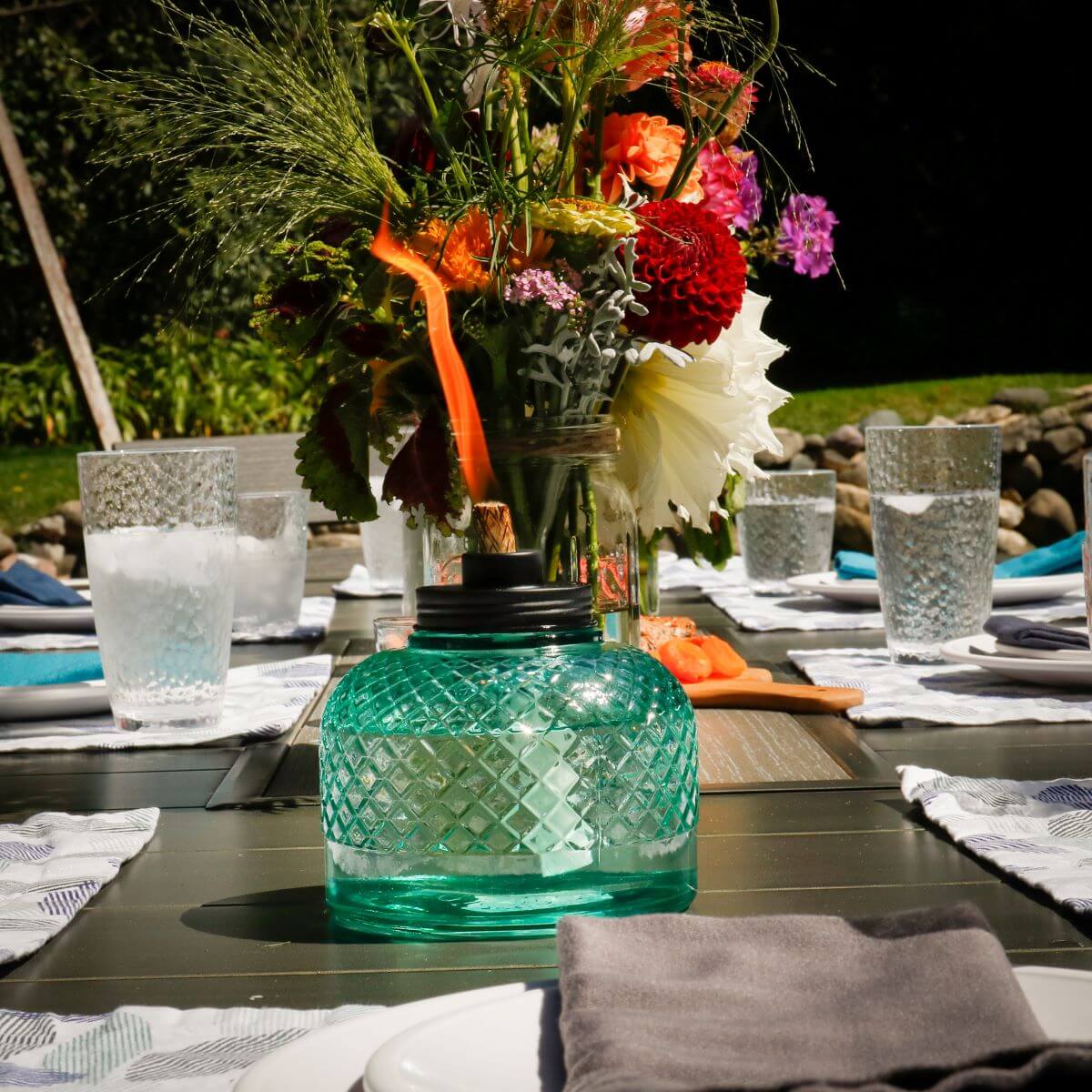 Green glass lantern with floral centerpiece on table setting.