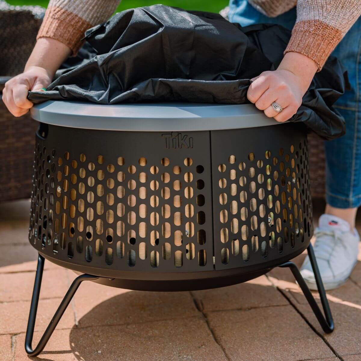 Dark gray Tiki fire pit with circular perforated design and black cover.