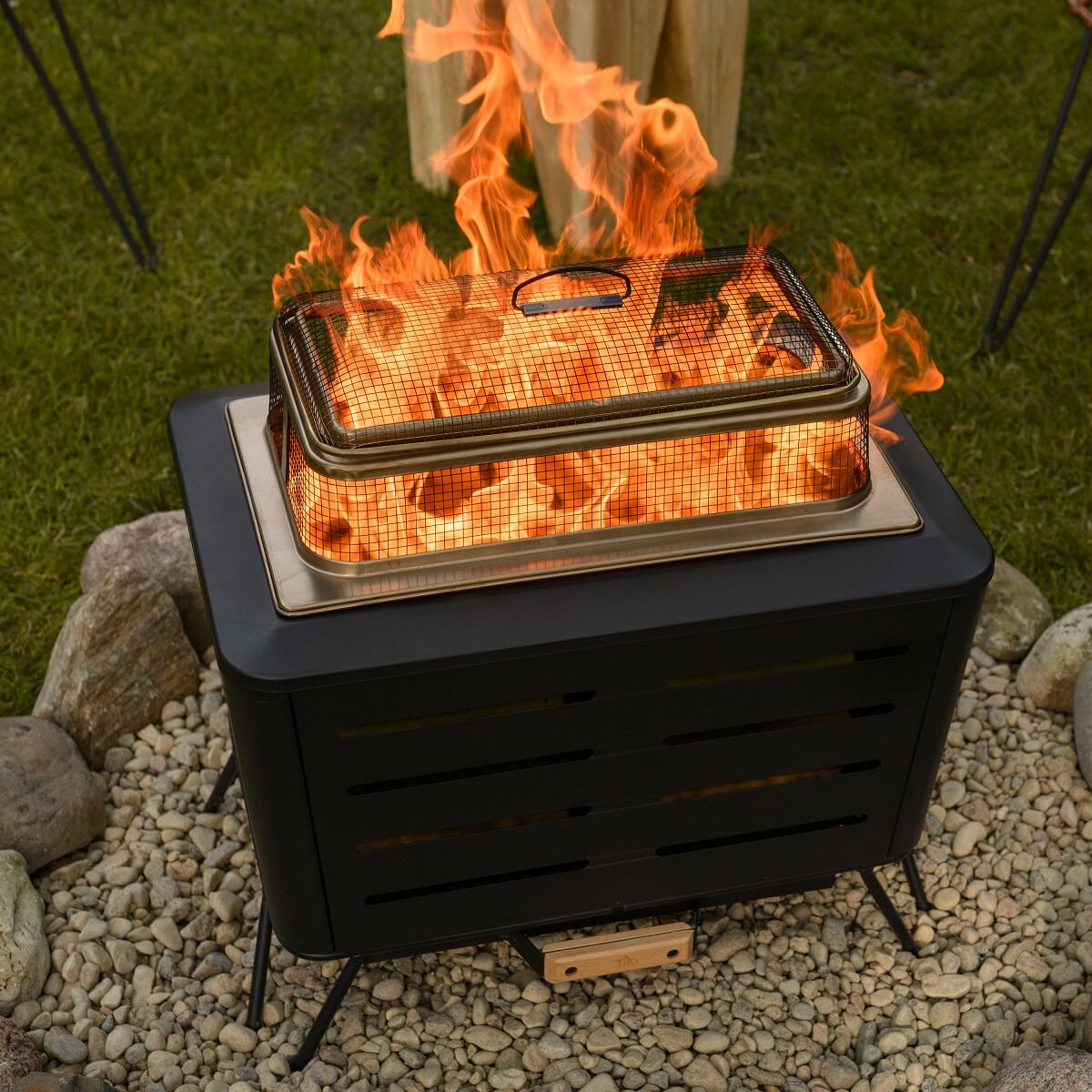 Black portable fire pit with mesh lid, glowing flames, outdoor setting.
