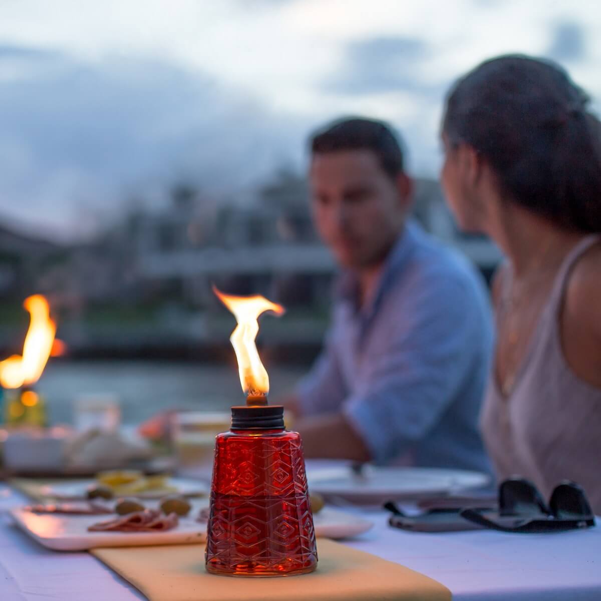 Red glass tiki torch with flame, set on dining table.