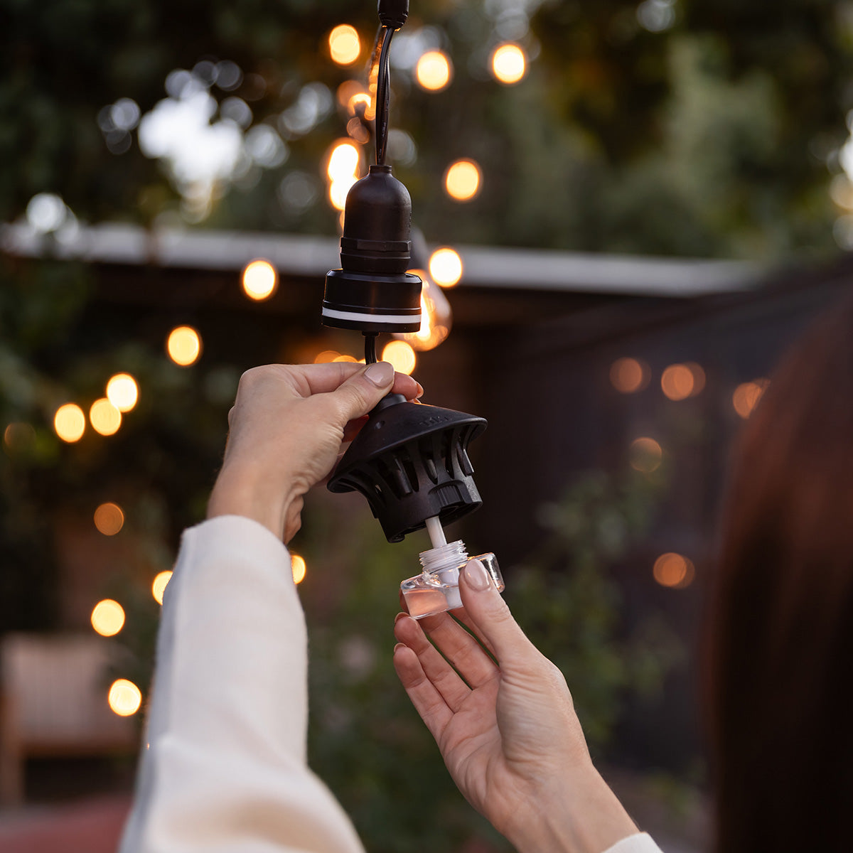 Black hanging light fixture with clear bulb holder, held by hands.