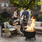 Black outdoor fire pit with roaring flames, surrounded by cozy patio furniture and people enjoying drinks.