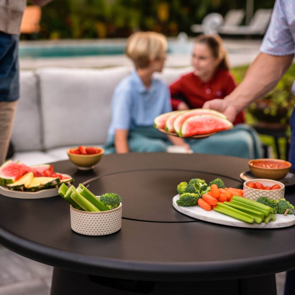Round black outdoor table with fresh fruit and vegetable platters.