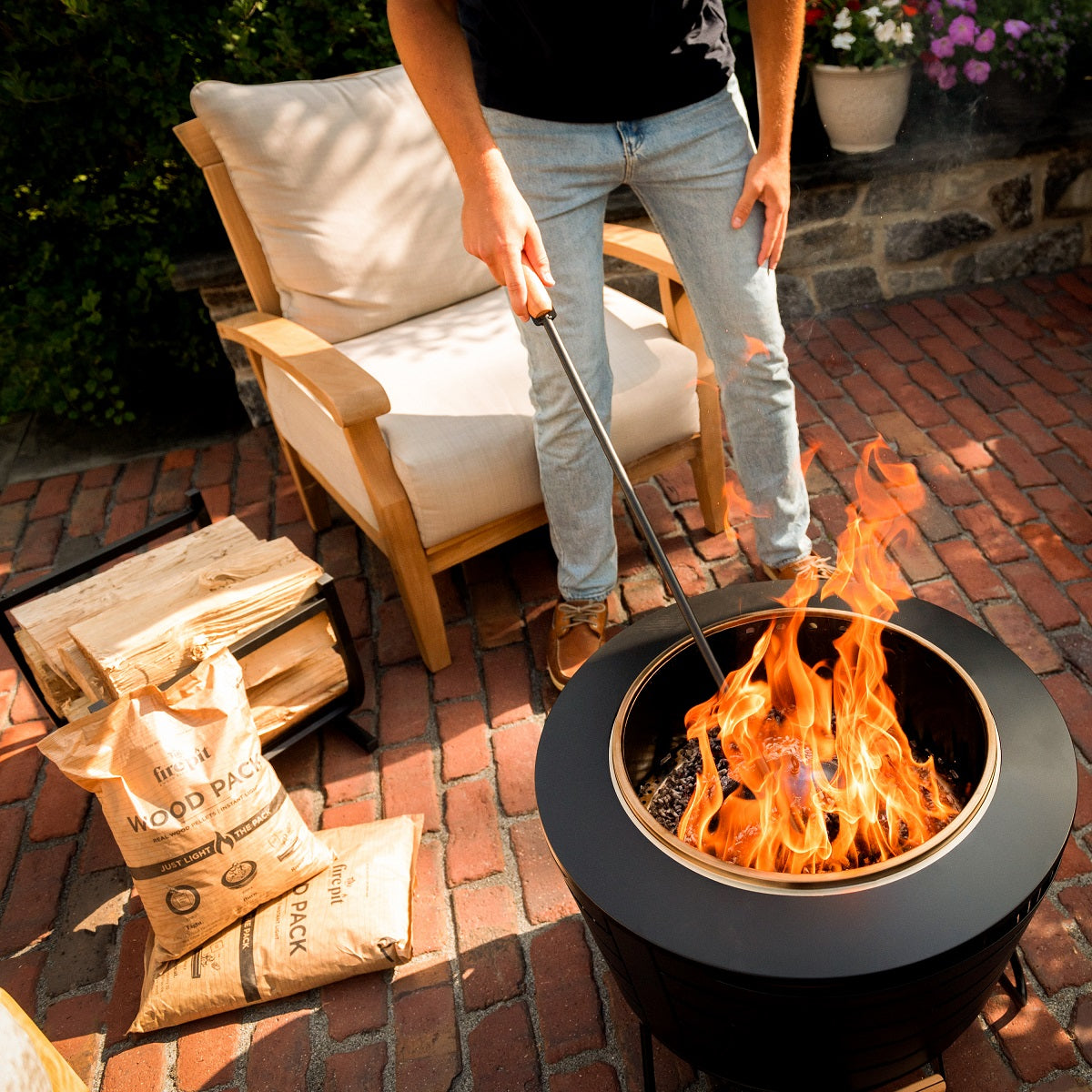 Black Fire Pit with flames, surrounded by Fire Pit Wood Packs and outdoor furniture.