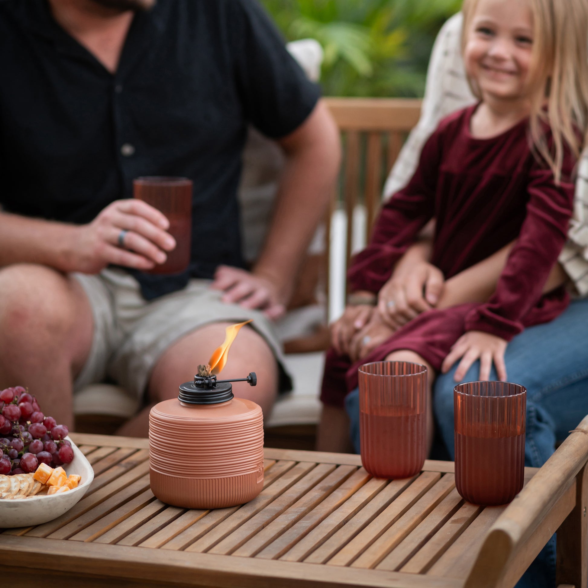 Terracotta tabletop lantern with flame, red cups, and snack bowl on wooden table.