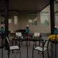 Outdoor patio set with glass table, white chairs, and teal tiki torches. Modern, accessible seating and decor.