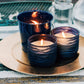 Three lit blue ceramic candles on a gold plate.
