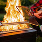Portable fire pit with mesh lid and flames, red plaid shirt in background.