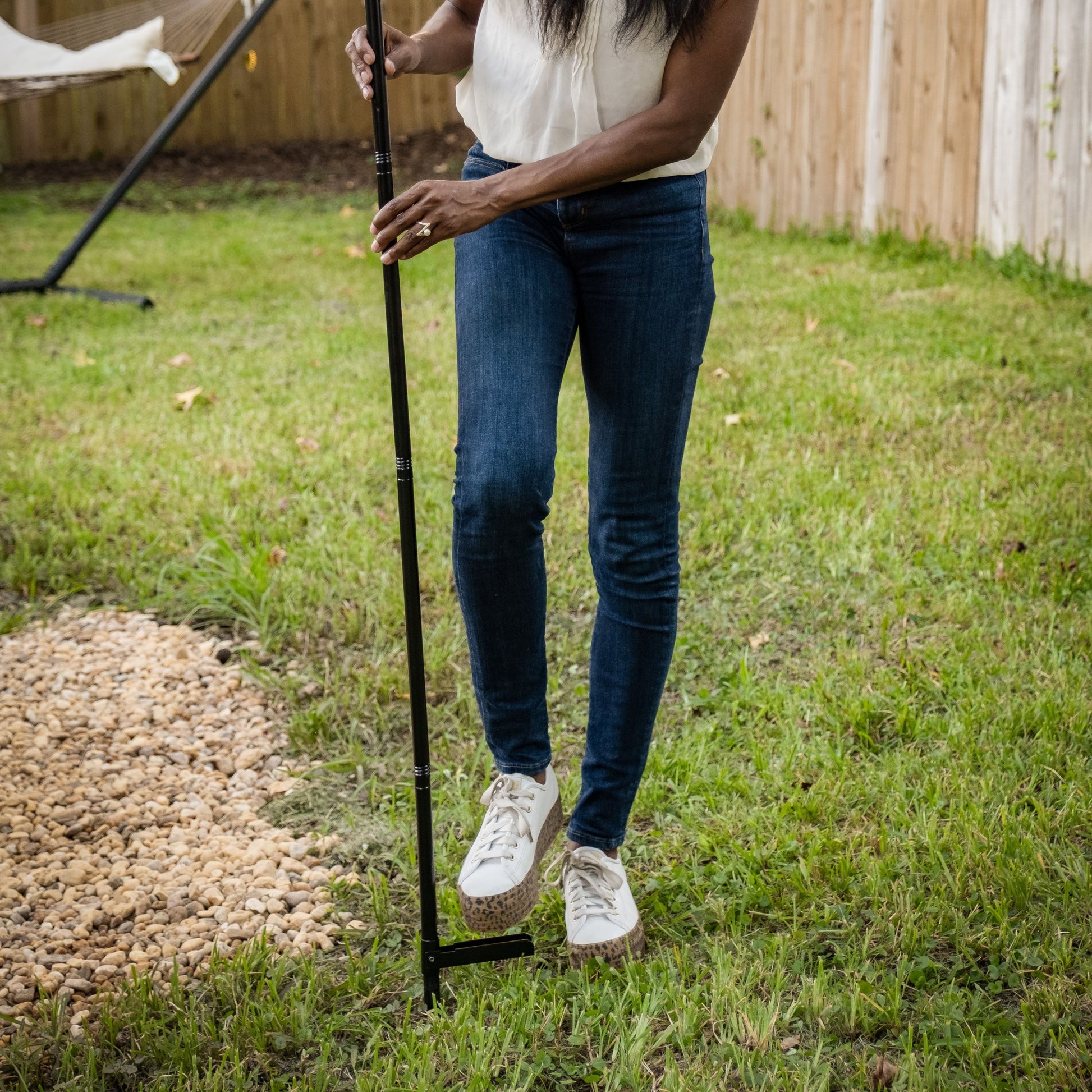 Black golf club held by person in white shirt, blue jeans, and white sneakers on grass.