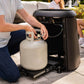 Black Tikr portable propane-powered patio heater with person connecting propane tank.
