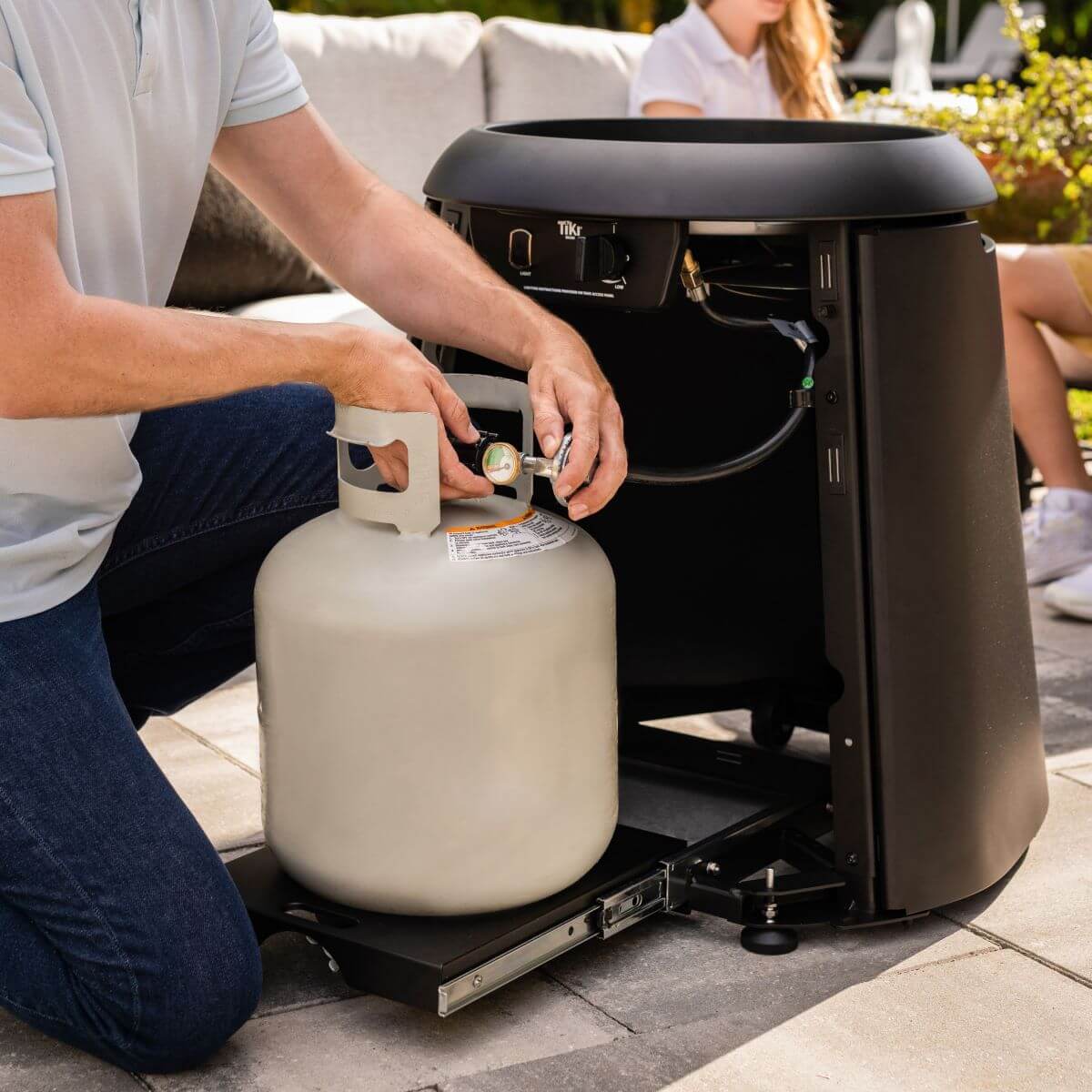 Black Tikr portable propane-powered patio heater with person connecting propane tank.