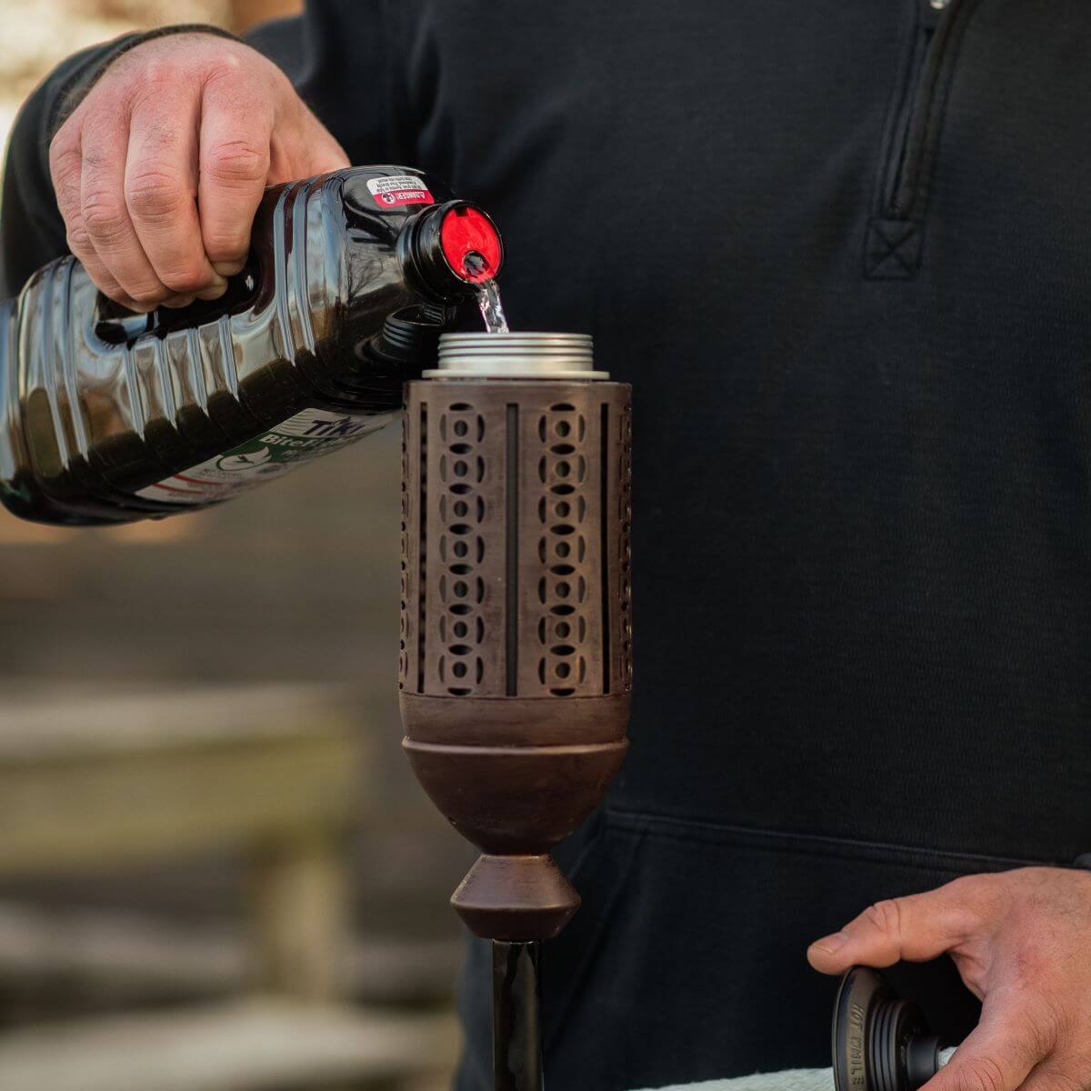 Dark wooden cocktail shaker with circular cutouts, being filled with a bottle of Tito's Handmade Vodka.