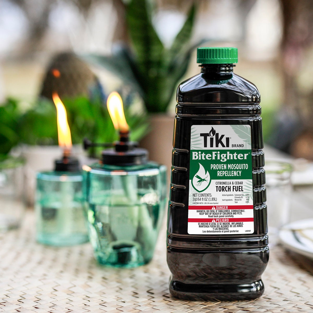 Green TIKI BiteFighter mosquito repellent torch fuel bottle with two lit glass torches.
