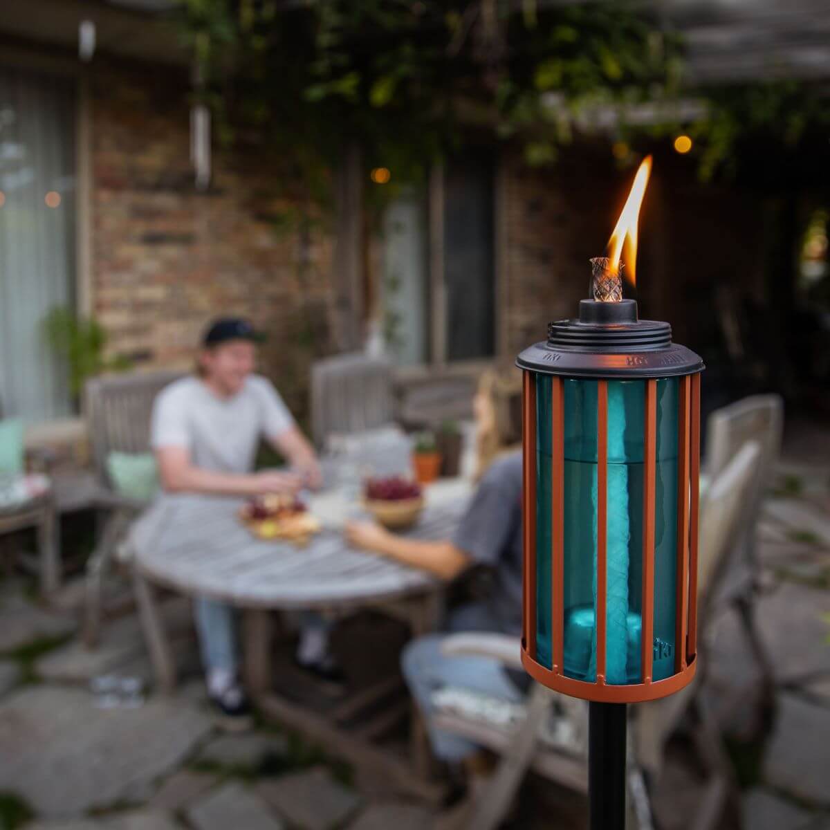 Blue and orange tiki torch with flame, outdoor setting.