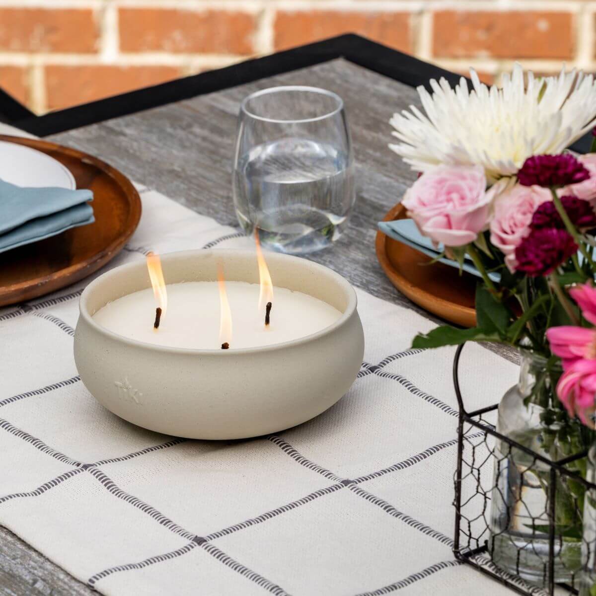 White ceramic candle with three wicks, placed on a table setting.