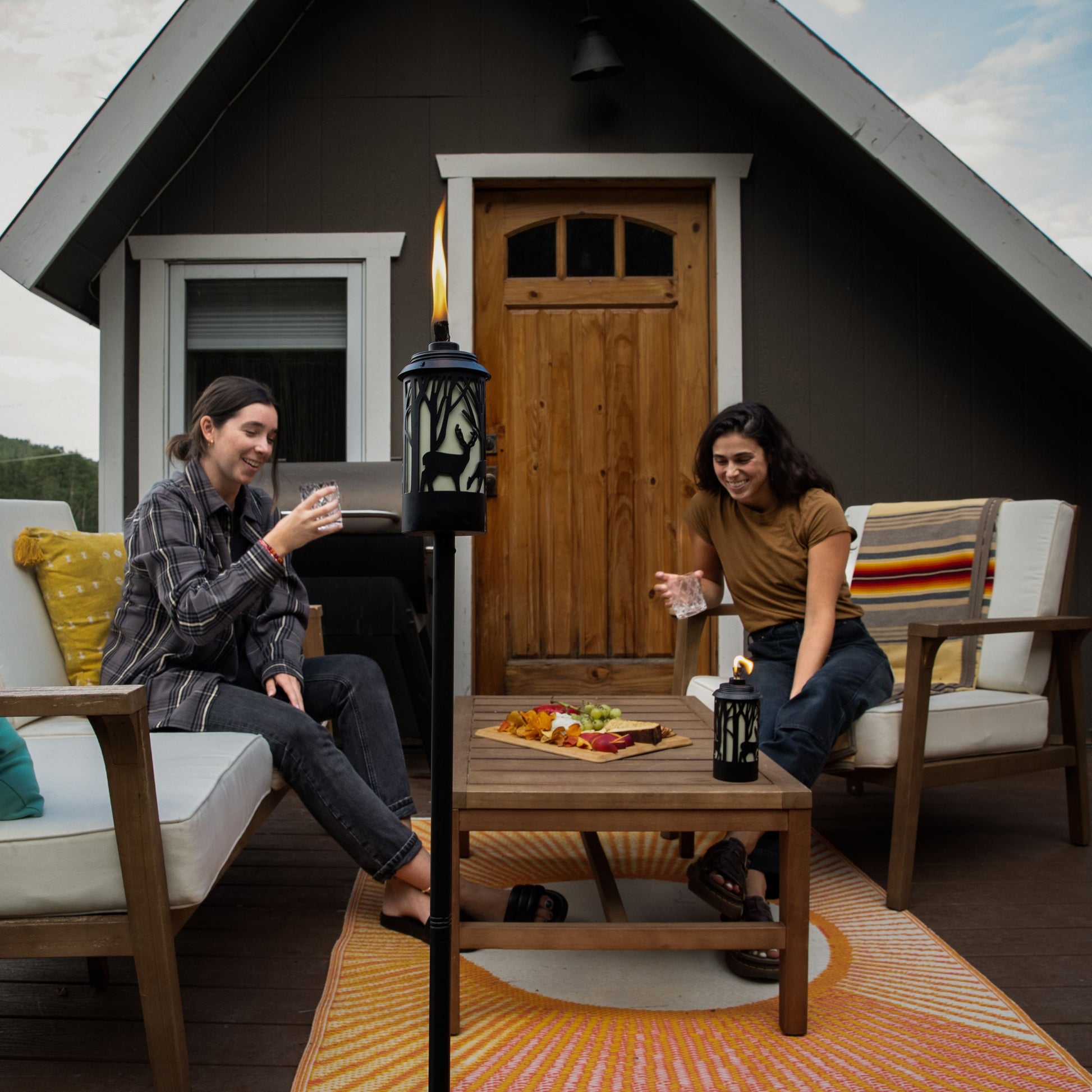 Black outdoor lantern with deer silhouette, emitting warm glow on patio setup.