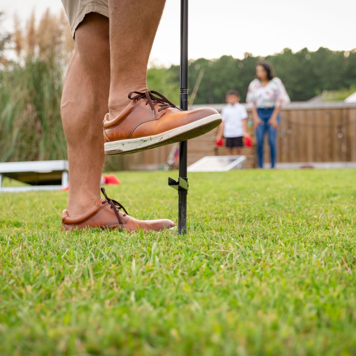 Brown leather dress shoes on grass near black pole.