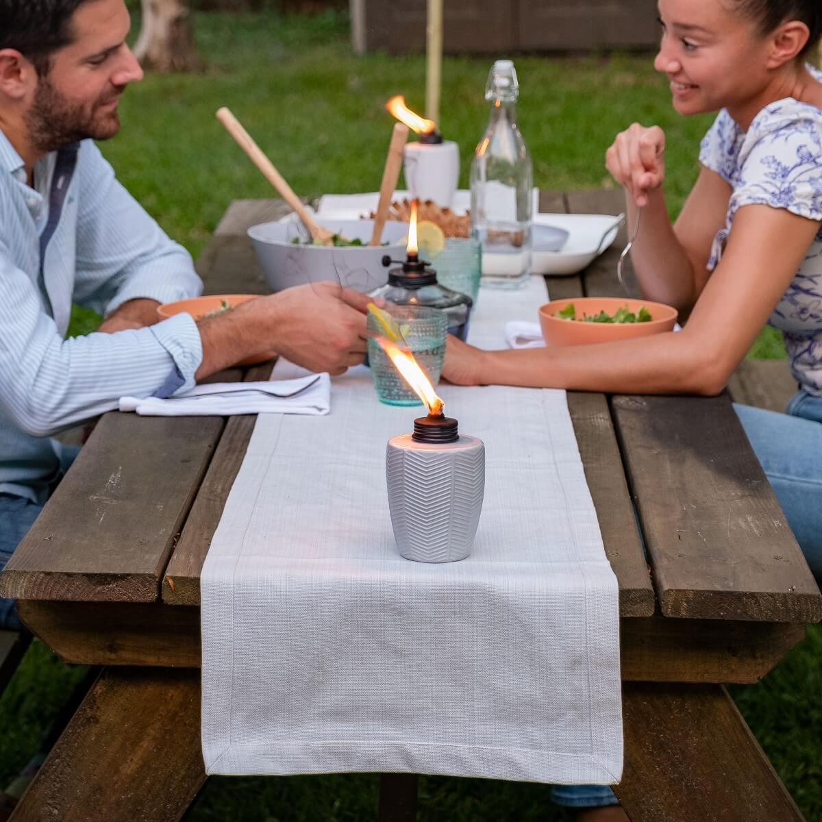 White textured ceramic oil lamp with flame, outdoor dining setting.