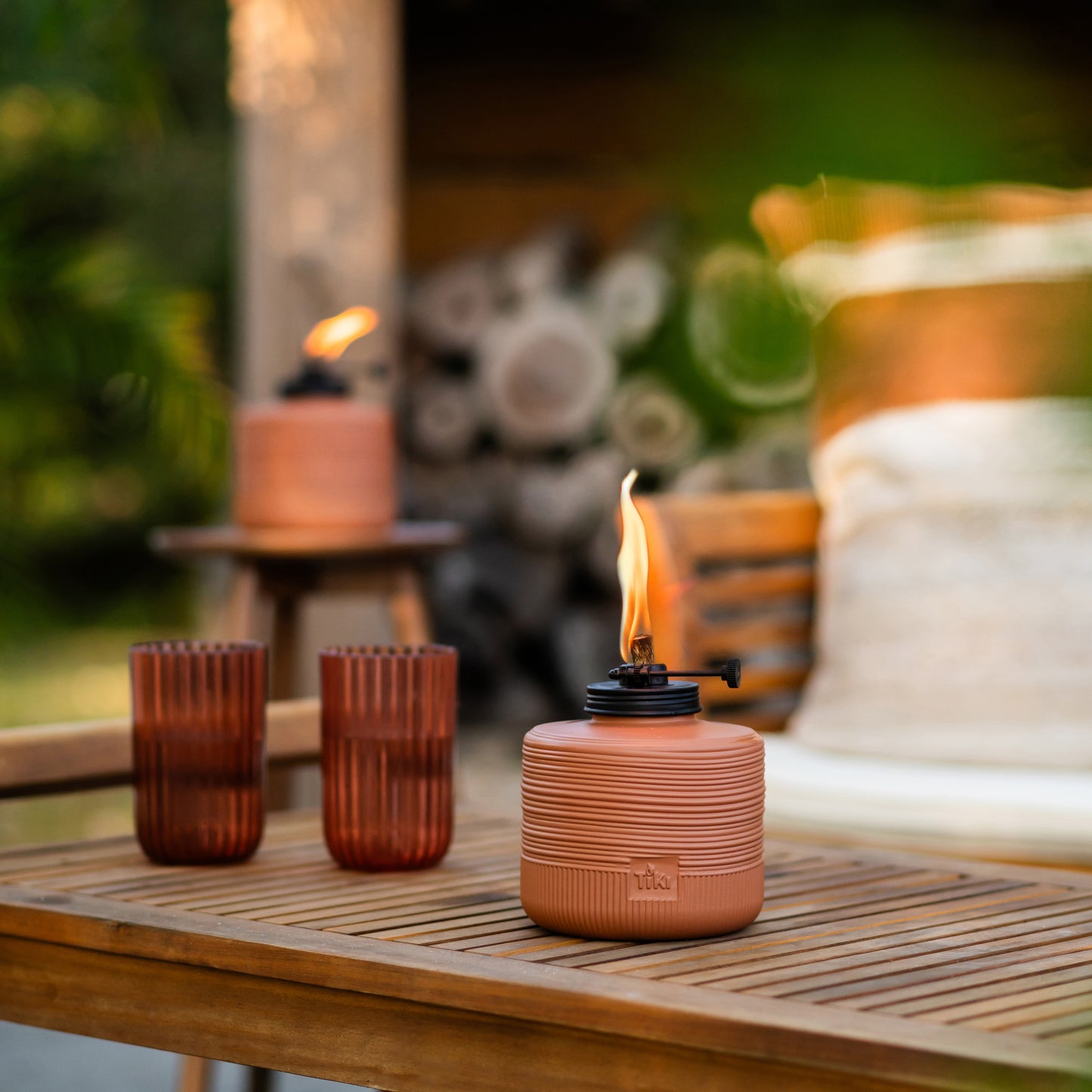 Orange TIKI lantern with flame, two red glasses, outdoor setting.