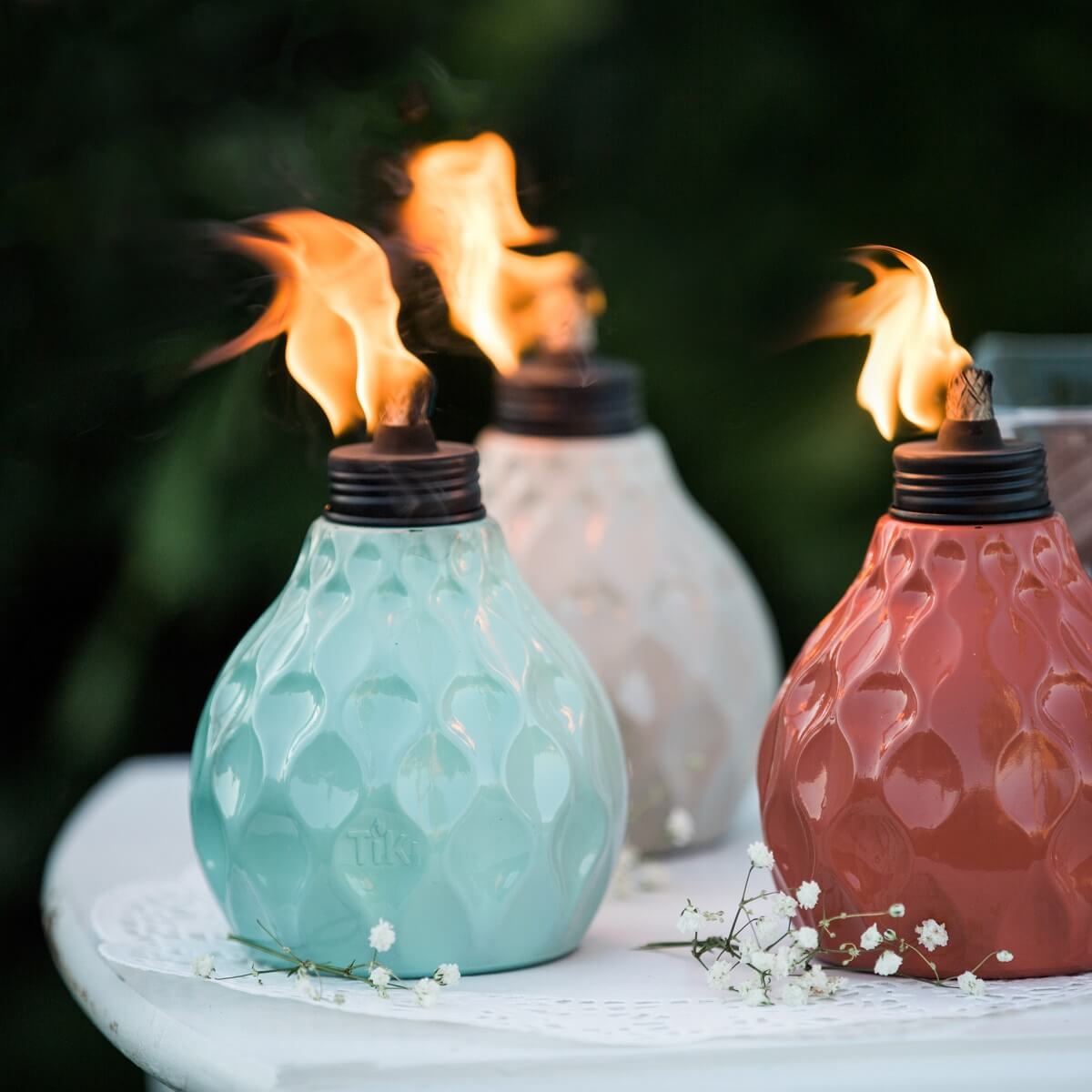 Tiki torches in blue, white, and red with flame, on lace tablecloth.