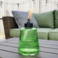 Green glass oil lamp with flame, outdoor setting.