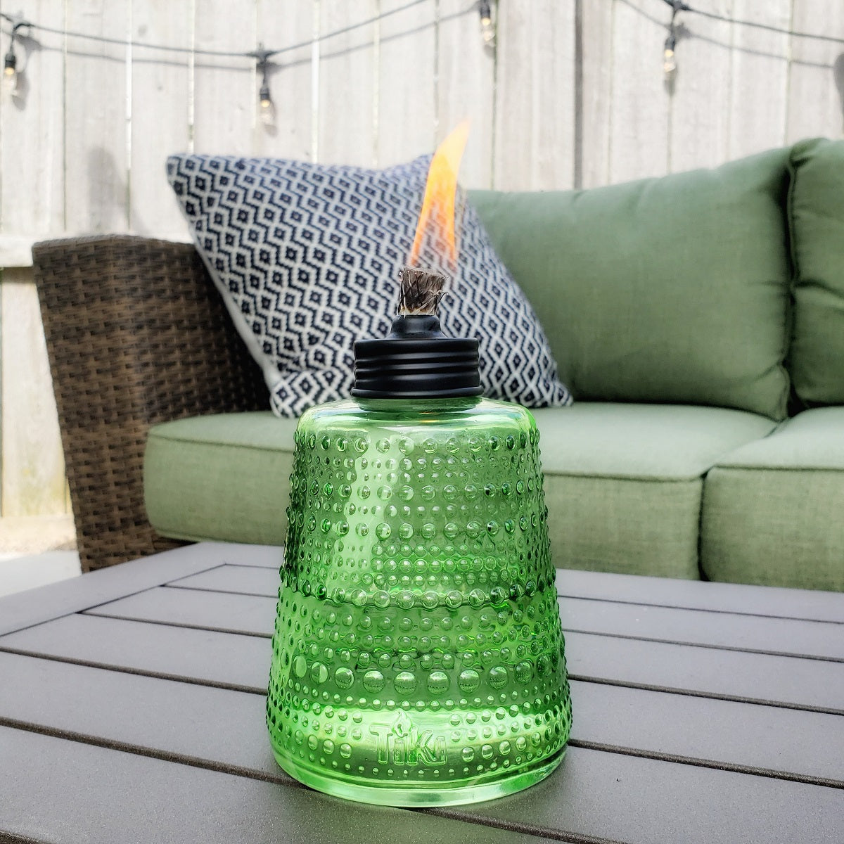 Green glass oil lamp with flame, outdoor setting.