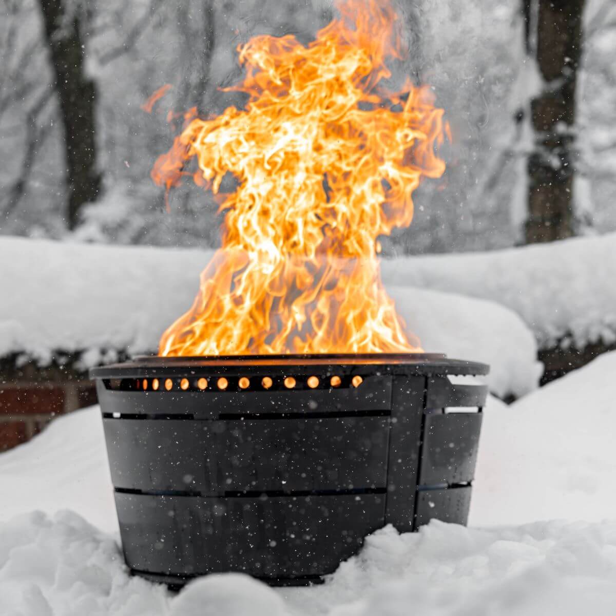 Black fire pit with roaring flames in snowy outdoor setting.