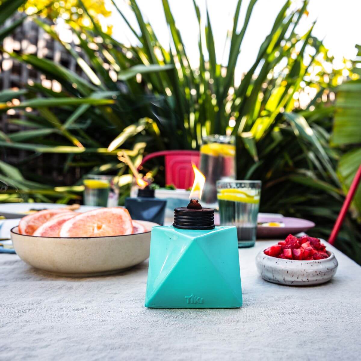 Teal Tika tabletop torch with flame, surrounded by outdoor dining setup.