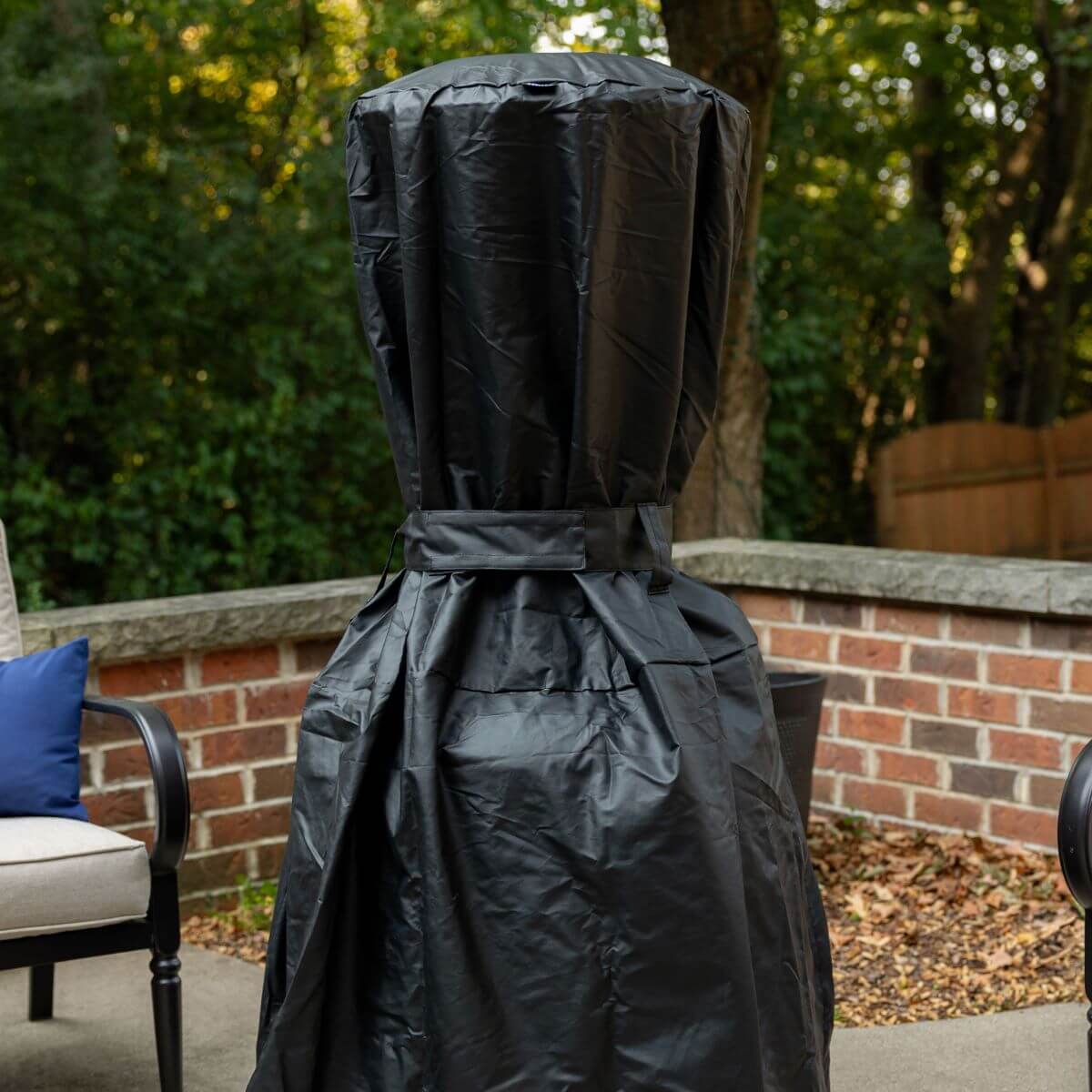 Black outdoor grill cover with adjustable strap, patio setting.