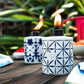White Tiki torch with blue geometric pattern, burning flame, outdoor setting.